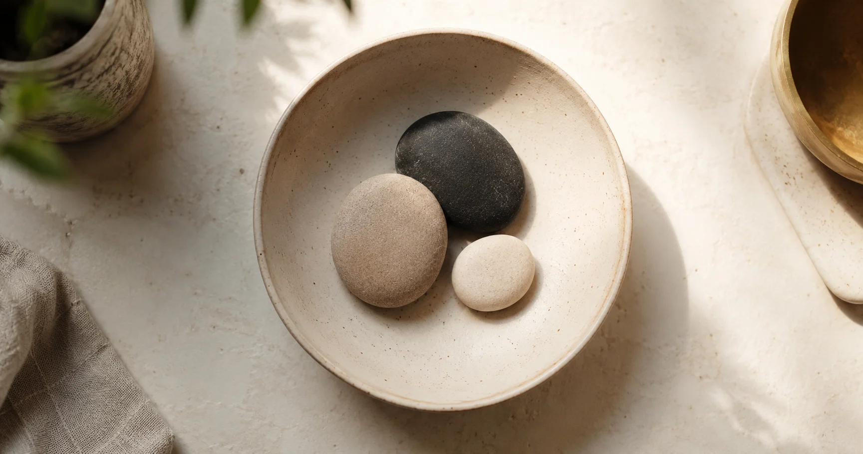 A simple ceramic bowl on a kitchen counter holding three pebbles of distinct sizes, soft natural light from above